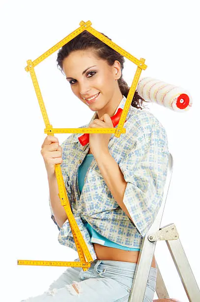 Closeup of beautiful woman with paint roller and meter creating house, sitting on ladder