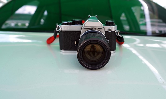A retro film camera with red strap isolated on a front body car backside a car glass.
