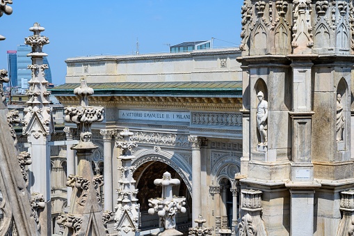 MIlan, Italy – June 18, 2023: Milan Cathedral close up of the various columns with the statues and artwork with the city and blue sky in background.