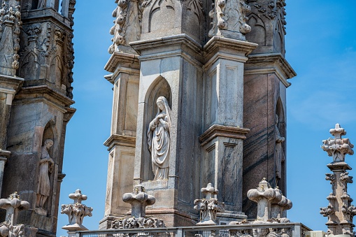 MIlan, Italy – June 18, 2023: Close-up of statue carved into the stone of the Milan Cathedral, roof top, on a summer day, with blue sky in background.