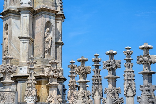 MIlan, Italy – June 18, 2023: Statue carved into the stone of the Milan Cathedral, roof top, on a summer day, with blue sky in background.