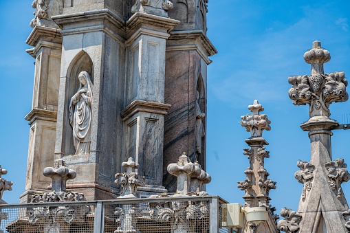 MIlan, Italy – June 18, 2023: Close-up of statue carved into the stone of the Milan Cathedral, roof top, on a summer day, with blue sky in background and the various artwork.