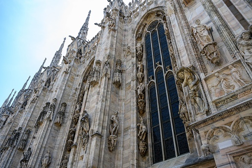 MIlan, Italy – June 18, 2023: The Milan Cathedral close-up of the windows and stone statues along the outside, with the blue sky on a summer day.