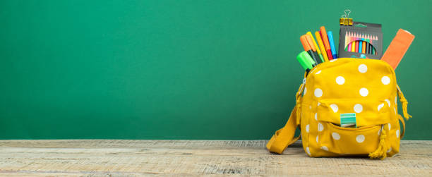 istock Backpack with different colorful stationery on table. Green background. Back to school. Banner design. 1728100166