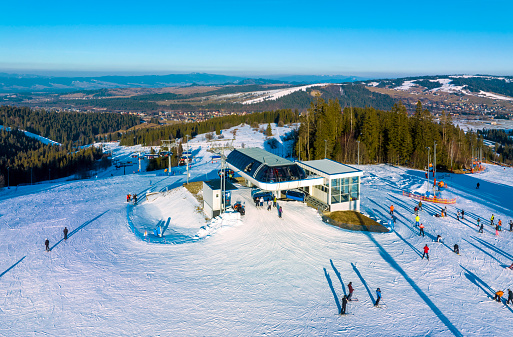 Ski slope, chairlift, skiers and snowboarders in Bialka Tatrzanska ski resort in Poland on Jankulakowski Wierch Mountain in winter. Aerial view in sunset light