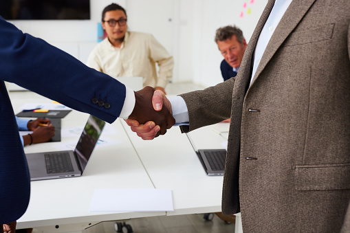 Midsection of male business professionals shaking hands with each other and sealing deal in corporate office