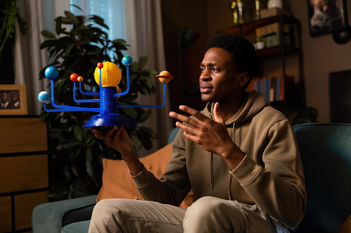 African American dark skinned guy in the photo appears confident and knowledgeable, as he holds a set of planets and shares his insights with the camera.