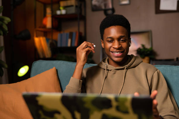 Curious delighted dark skinned black guy in cozy living room participating in a virtual meeting or video conference, listening to and communicating with other participants