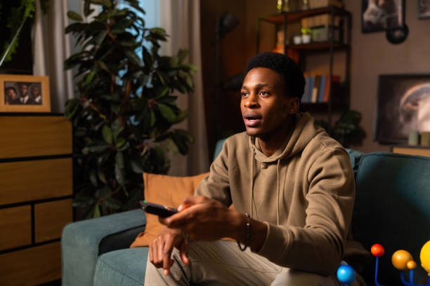 istock Dark-skinned man holding a remote control, symbolizing his authority over his entertainment choices and setting the tone for a cozy evening 1728171603