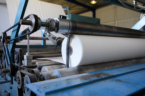 Close-up of roll winding machine. Greek factory for the production of paper rolls for hygiene. Manufacture of paper towels and toilet paper. Selective soft focus
