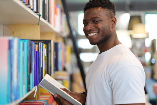istock A joyful young man in a university library, surrounded by bookshelves, selects books with a smile, exuding intelligence. 1728208141