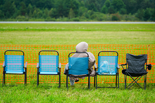 Folding chairs with a lone spectator at the edge of a green field waiting for the show to start, orange plastic temporary portable fence, rear view