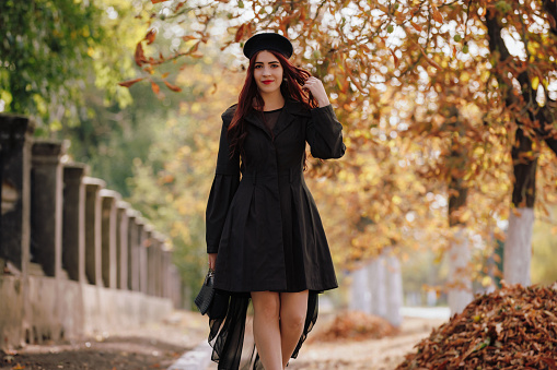 A girl in black retro coat french style walks along alley in the autumn park