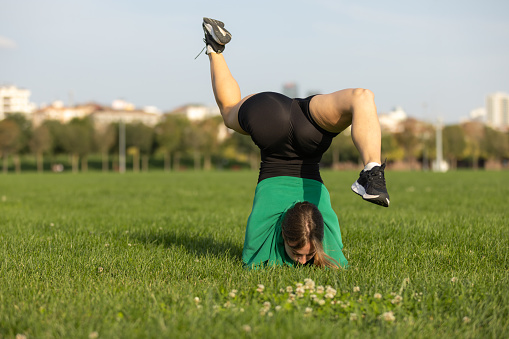 Pretty young woman is stretching on the grass at public area.