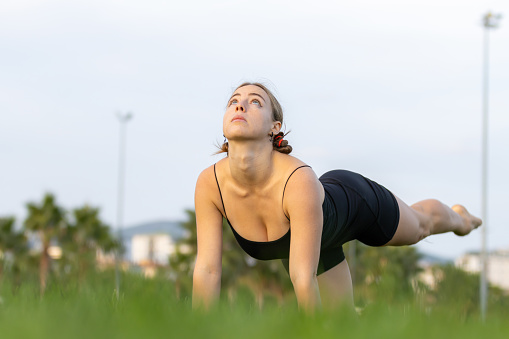 Flexible young athlete lady is exercising on the grass.