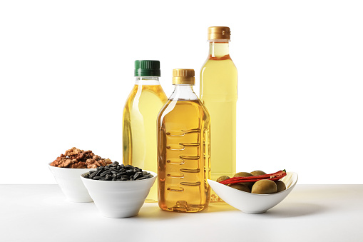 Bottles of different cooking oils, sunflower seeds, walnuts and olives on white background