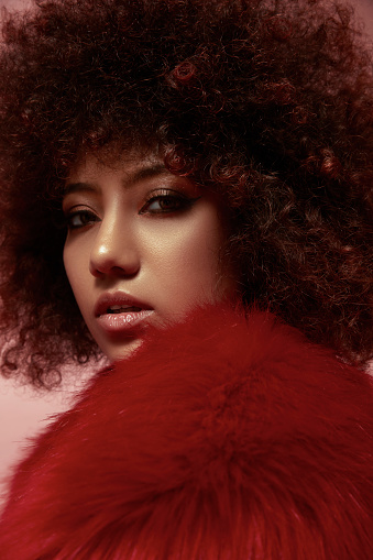 Curly-haired mixed race young woman in a red fur coat.