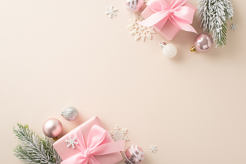 Glitzy Winter Wonderland: Top view of pink present boxes, cute tree trinkets, glistening balls, icy snowflakes, frosty evergreen twigs on subtle beige base. Space for New Year's wishes or advertising