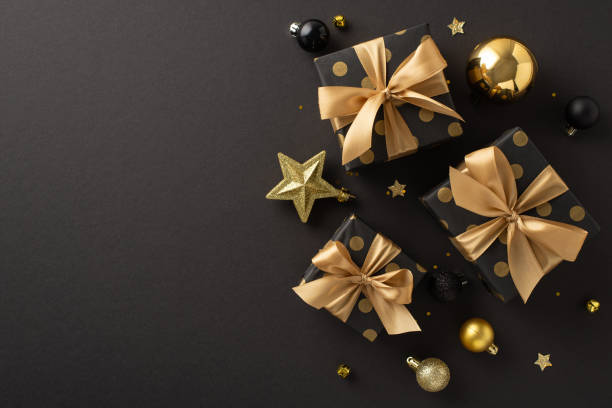 istock Luxe Noel blessings inspiration. Overhead view of opulent present boxes, extravagant tree decorations, golden and black balls, twinkling confetti on a black background with space for greetings or ads 1728335078