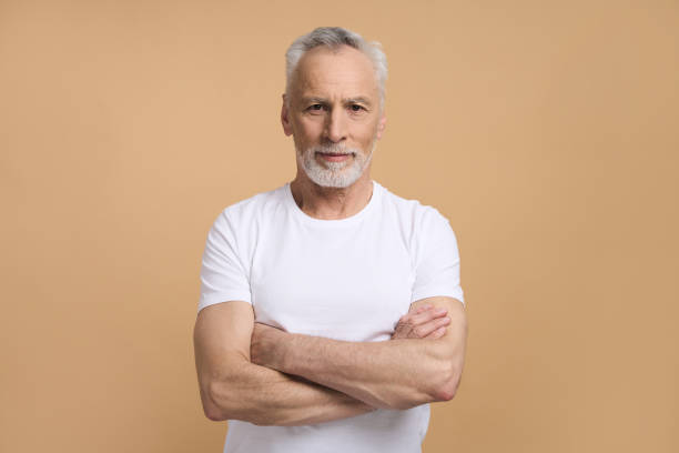 istock Caucasian retired senior man smiling at camera, posing with arms folded isolated on beige background 1728335180