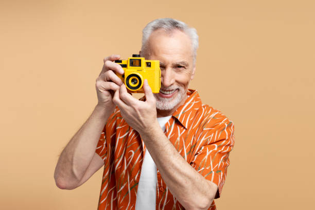 셔츠를 입고 사진을 찍고 있는 60세 남성이 파란색 배경에 격리된 카메라를 사용하여 행복한 미소를 짓고 있다 - 60 65 years 뉴스 사진 이미지
