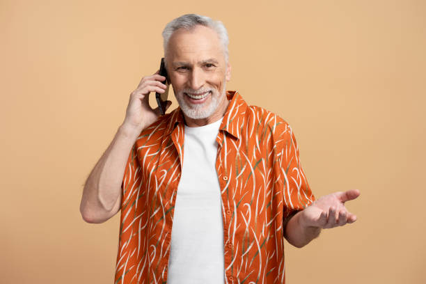 istock Smiling gray haired pensioner using smartphone isolated on beige background, looking at camera 1728335257