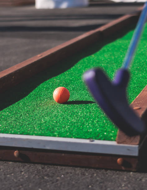 istock Mini golf course, process of playing miniature golf on a green artificial turf in a summer sunny day, eqipment for mini-golf in a golf club resort, club and ball 1728341095
