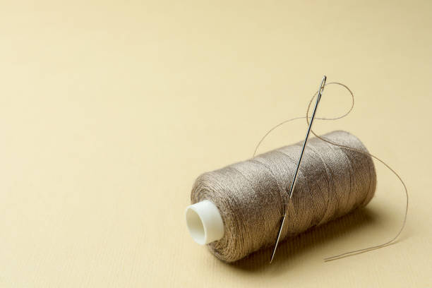 istock Spool of grey sewing thread with needle and thimble on beige background. Space for text 1728352272