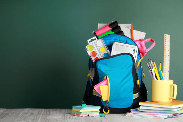 istock Backpack with different school stationery on wooden table near chalkboard, space for text 1728353669