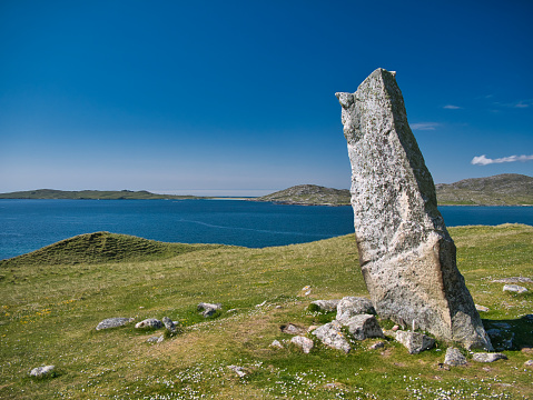 The 3m high MacLeod's Stone on the machair on the Atlantic coast of the Isle of Harris in the Outer Hebrides, Scotland, UK. The island of Taransay can be seen behind.