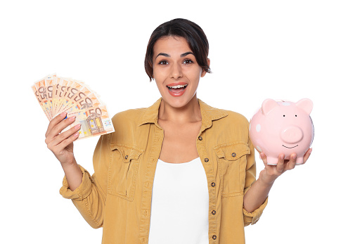 Excited young woman with money and piggy bank on white background