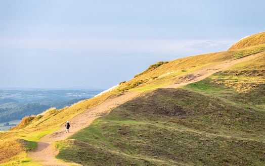 An anonymous human figure ascending the main hill walking pathway leading up the south side of the Beacon,to summit of the ancient Iron Age hill fort,on sunny summer afternoon,near to sunset.