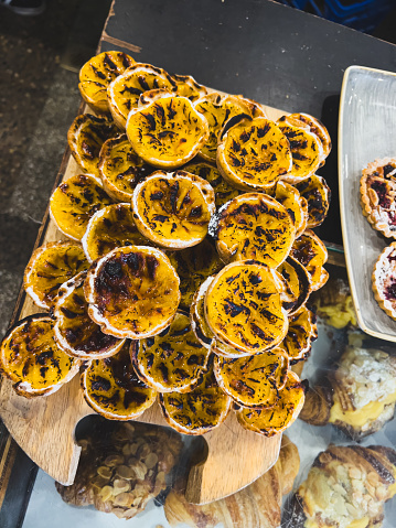 Vertical high angle closeup photo of Portuguese custard tarts, on a wooden board, freshly baked in a wood fired oven, on sale in a Cafe Bakery. Armidale, NSW.