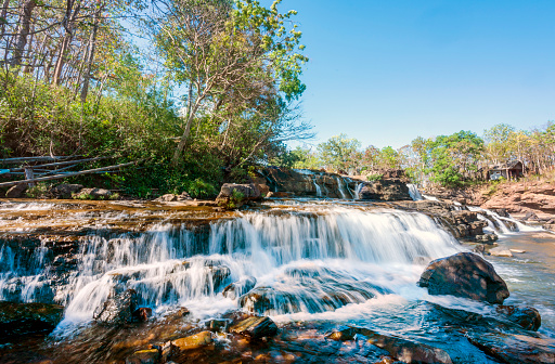 On the Bolaven Plateau of southern Laos,located close to the tiny village of Tad Lo,beautiful medium sized tiered waterfallls and sunlit boulders in the foreground.