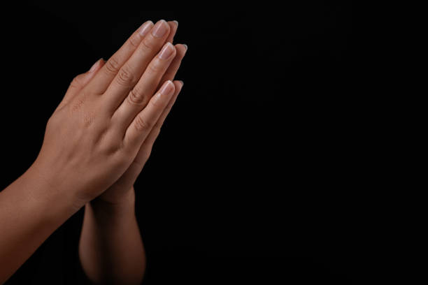 istock Woman holding hands clasped while praying against black background, closeup. Space for text 1728399925