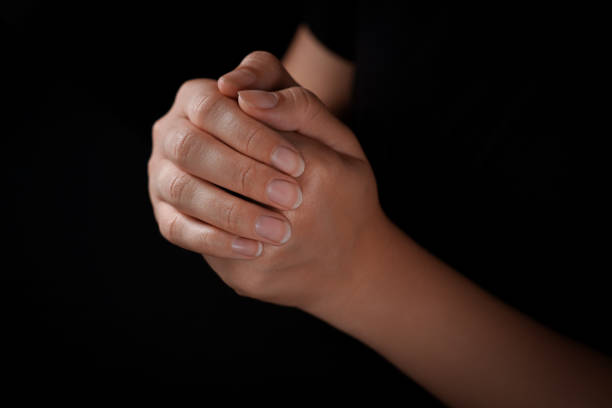 istock Woman holding hands clasped while praying against black background, closeup 1728400664