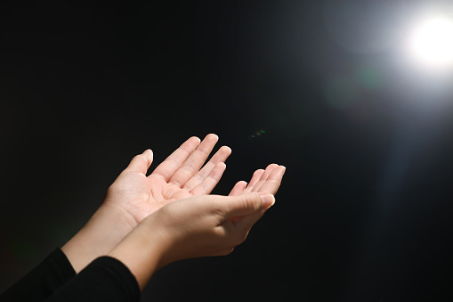 Woman stretching hands towards light in darkness, closeup