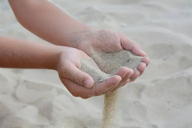 Child pouring sand from hands on beach, closeup. Fleeting time concept