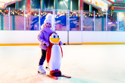 A little girl is skating on an ice rink, holding on to a support, a child is learning to skate, winter entertainment for children.