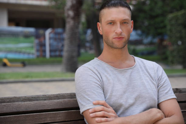 istock Handsome young man sitting on bench in park, space for text 1728452486