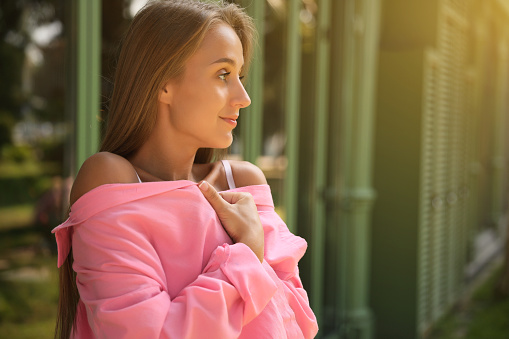 Beautiful young woman in stylish pink shirt near building outdoors, space for text