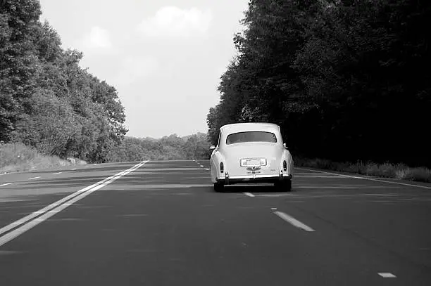 Vintage Rolls Royce car driving down an open road.