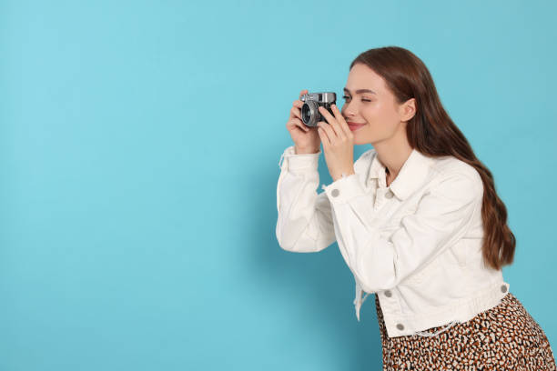 istock Young woman with camera taking photo on light blue background, space for text. Interesting hobby 1728463740