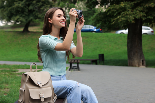 Young woman with camera taking photo in park. Interesting hobby