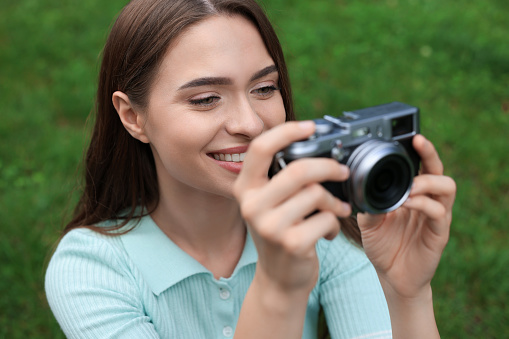 Young woman with camera taking photo outdoors. Interesting hobby