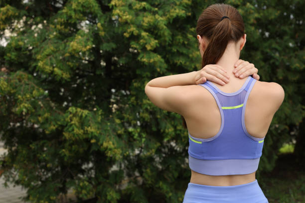 Young woman suffering from neck pain outdoors, back view. Space for text