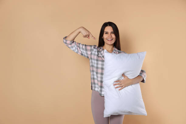 istock Happy young woman pointing at soft pillow on beige background, space for text 1728467083