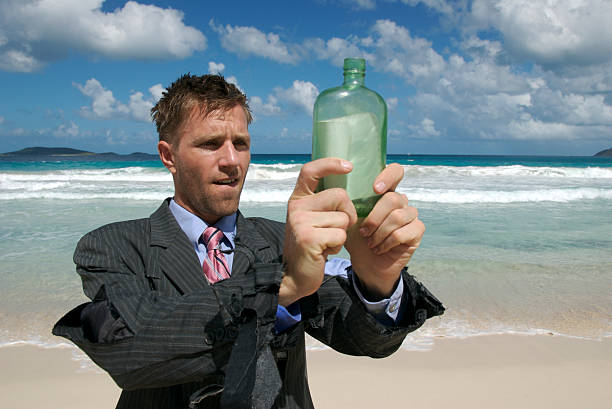 изгой бизнесмен, держа послание в бутылке на тропический пляж - message in a bottle beached bottle desert island стоковые фото и изображения