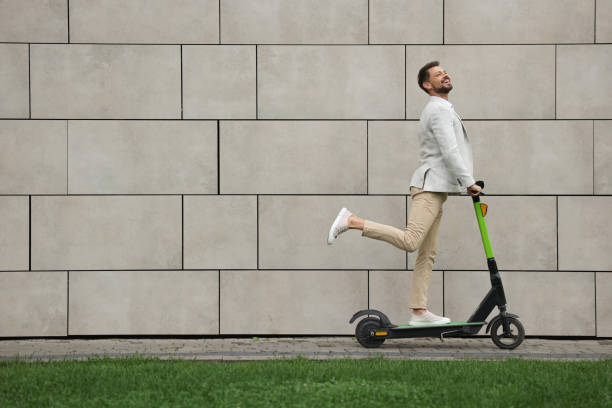 istock Businessman riding modern kick scooter near grey stone wall outdoors, space for text 1728473453