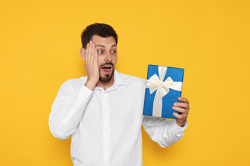 Surprised man with gift box on yellow background
